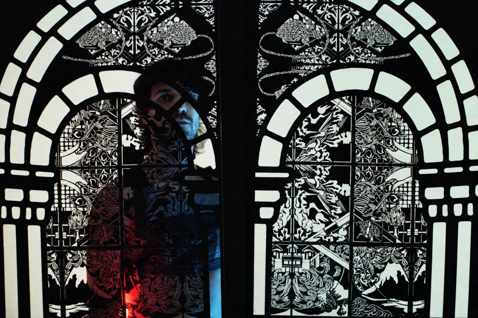 A participant stands partially concealed behind a FableType light-cutting panel, with the intricate paper design framing the face against an illuminated backdrop.
